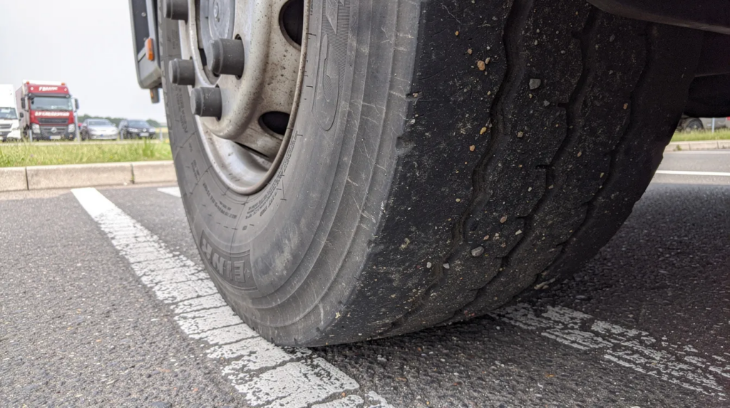 31f3a8d8-3f0b-4d0e-870b-7aa0eb741844 – LKW Help 24 Die Nahaufnahme zeigt einen großen LKW-Reifen auf einem Autobahnrastplatz bei Tageslicht, der mit seiner robusten Struktur und den markanten Seitenwänden die Eigenschaften eines verstärkten XL-Reifens hervorhebt. Informationen über die Tragfähigkeit und den Druck sind auf der Reifenflanke sichtbar, was für Autofahrer und Fahrzeughersteller von Bedeutung ist.