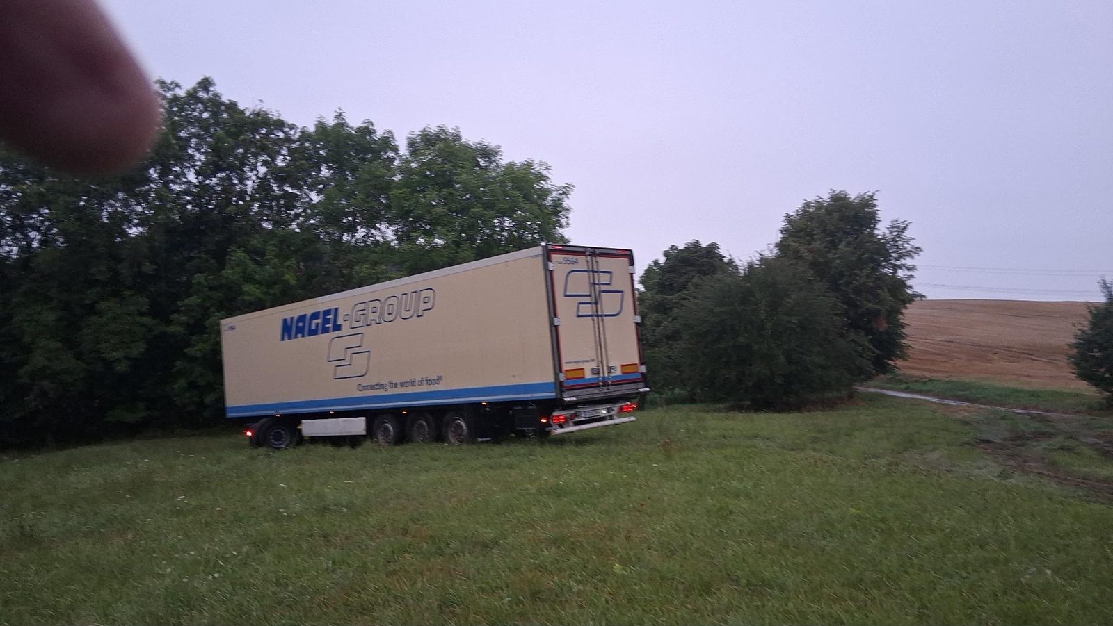 Kühlauflieger steht schräg auf der durchnässten Wiese bei Dämmerung und Regen, der LKW Abschleppdienst beginnt die Bergung