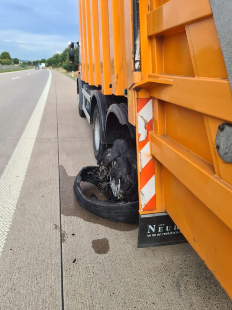 Reifenpanne in der Nähe: komplett zerrissener Hinterreifen an einem orangefarbenen Entsorgungsfahrzeug auf dem Standstreifen