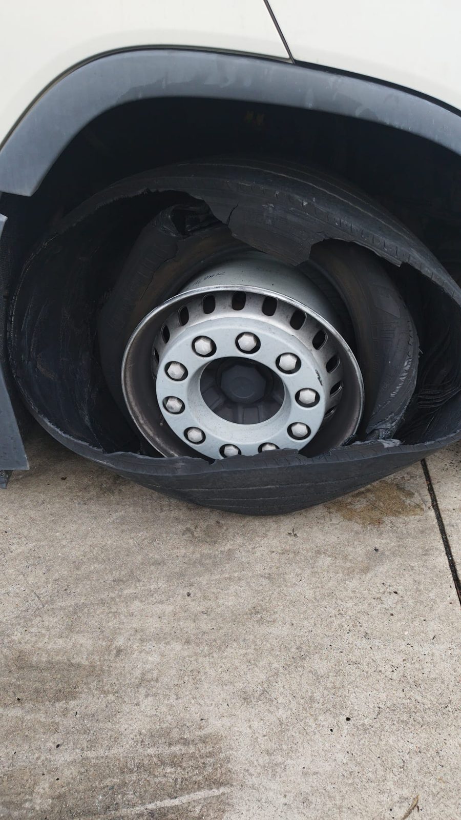 Truck tyre burst: shredded tread hanging in the wheel arch of a white coach, steel rim undamaged