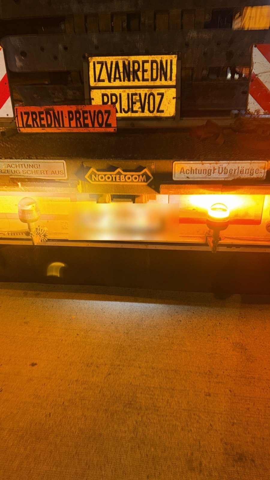 Serwis opon TIR Niemcy: tył naczepy Nooteboom nocą z lampami ostrzegawczymi i tablicami transportu ponadgabarytowego